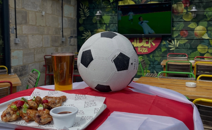 people cheering around a table watching rugby, with a bucket of beer bottles on the table